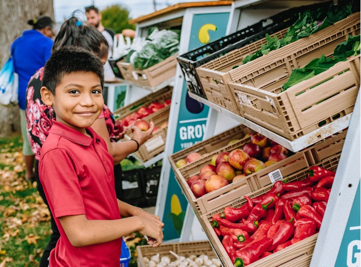 Shalom Farms | Young boy standing in front of boxes of produce at market